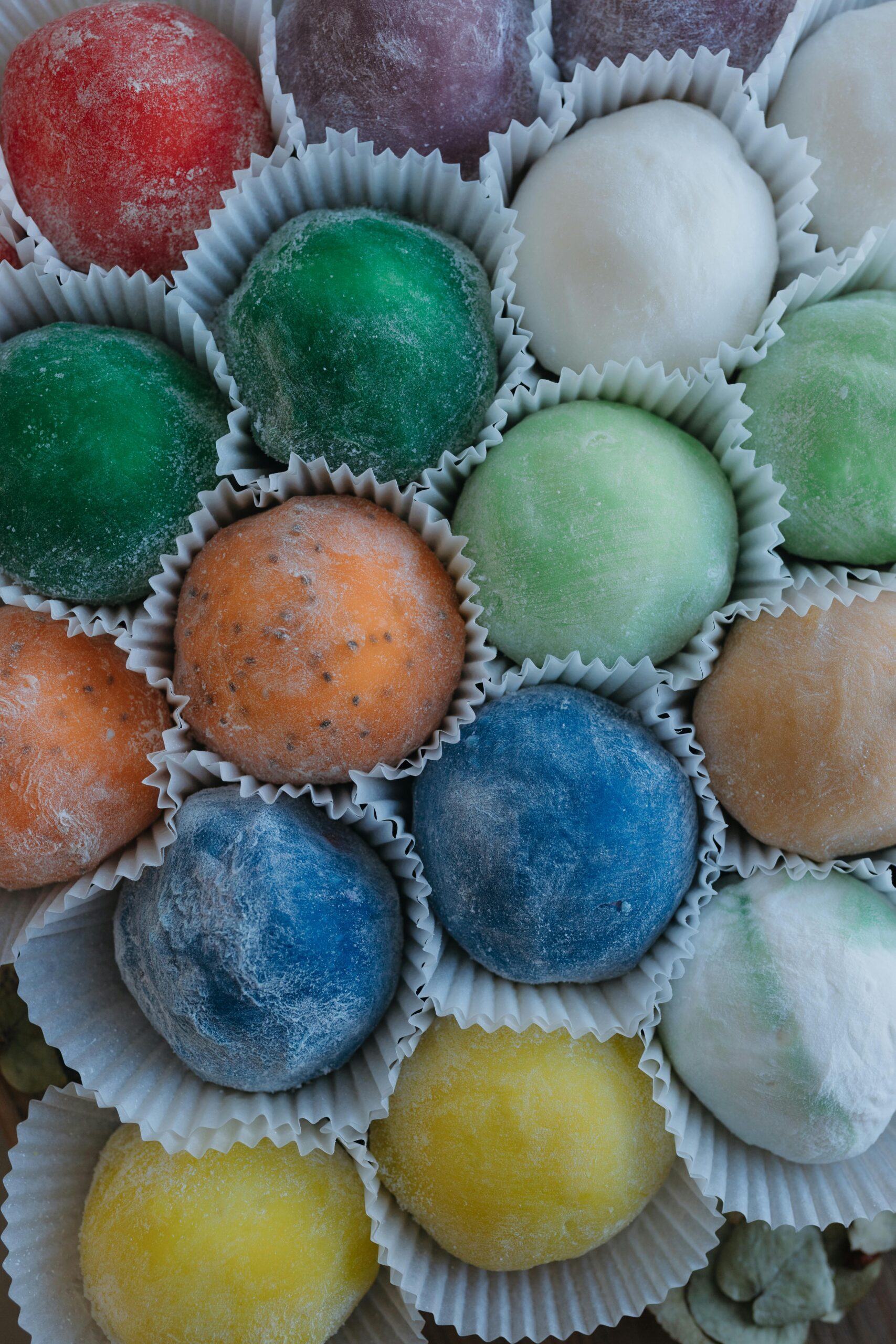 Vibrant mochi balls in various colors arranged in paper cups, showcasing their texture.