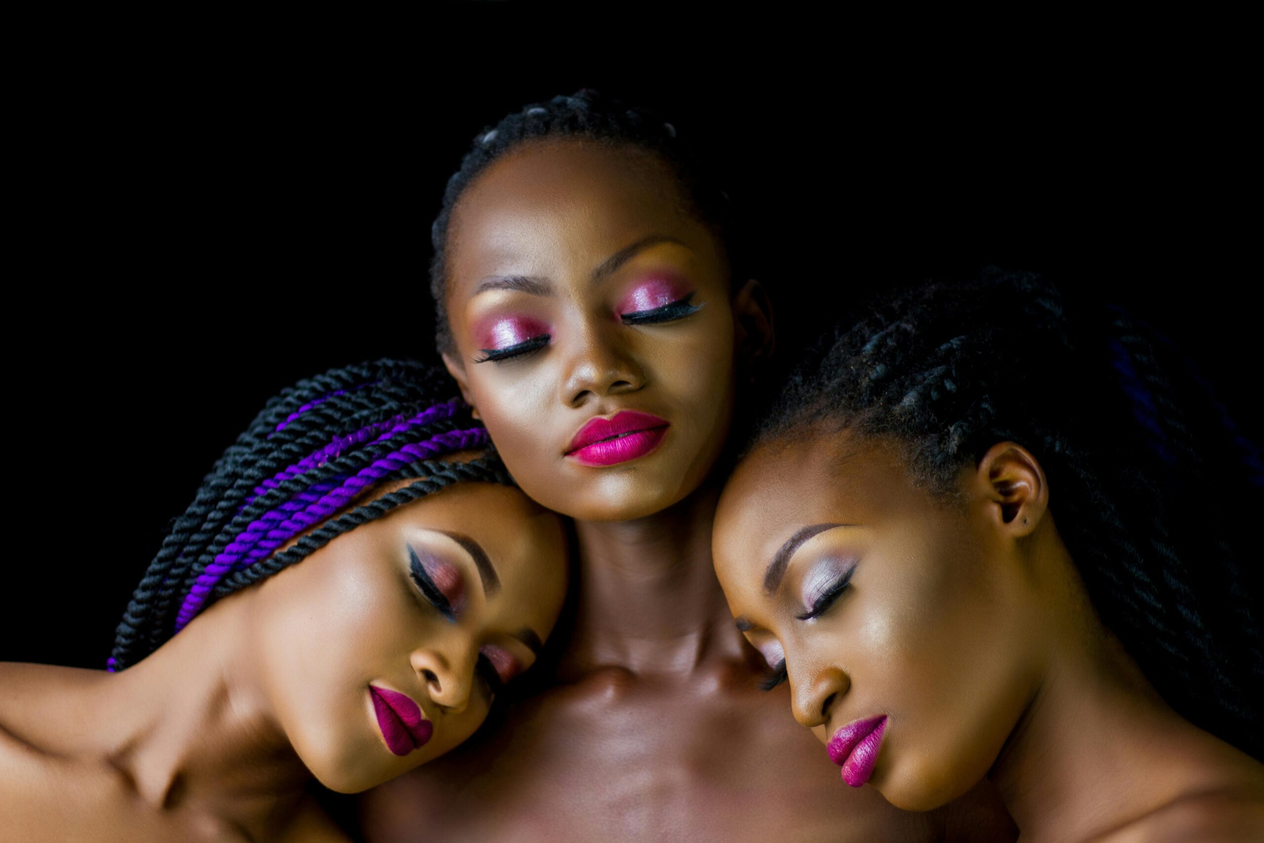 A captivating studio portrait of three women showcasing elegant makeup and braided hairstyles.
