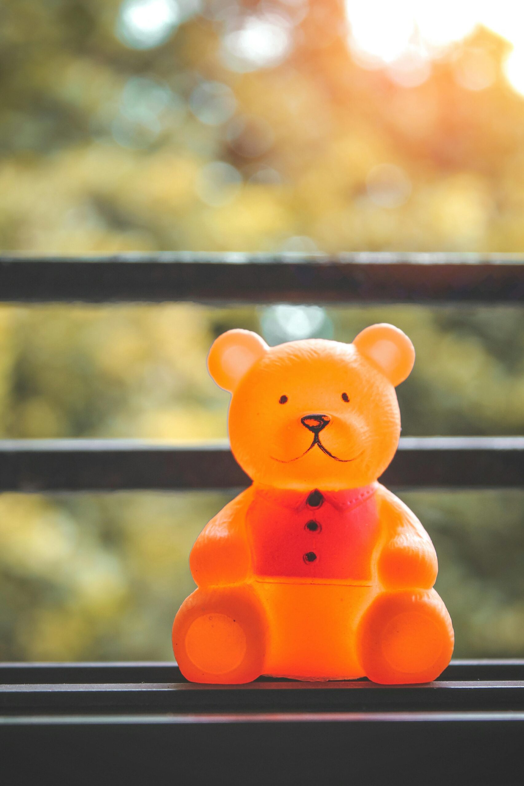 Adorable teddy bear toy on a ledge with sunlit bokeh background. Perfect for children's themes or playful settings.